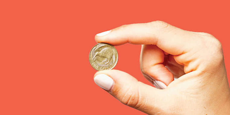 A hand holding a $1 NZ coin